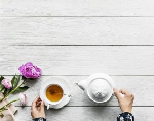 person holding teapot and teacup at an outdoor patio table