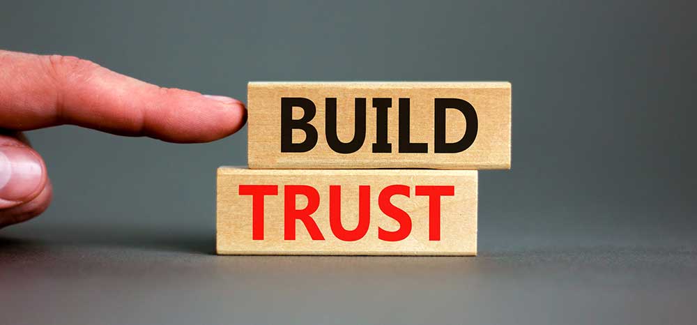 Hand pointing at wood blocks with the words "Build Trust"